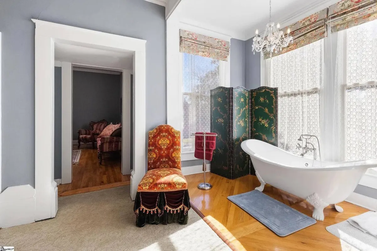 A tranquil, elegant bathroom featuring a freestanding bathtub, an ornate chair, and a decorative screen. The chandelier overhead adds a touch of luxury, while the room's layout encourages relaxation and unwinding after a long day. The space feels inviting for both a restorative soak and quiet moments of solitude.